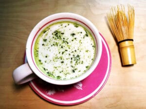 cup of matcha latte with matcha whisk